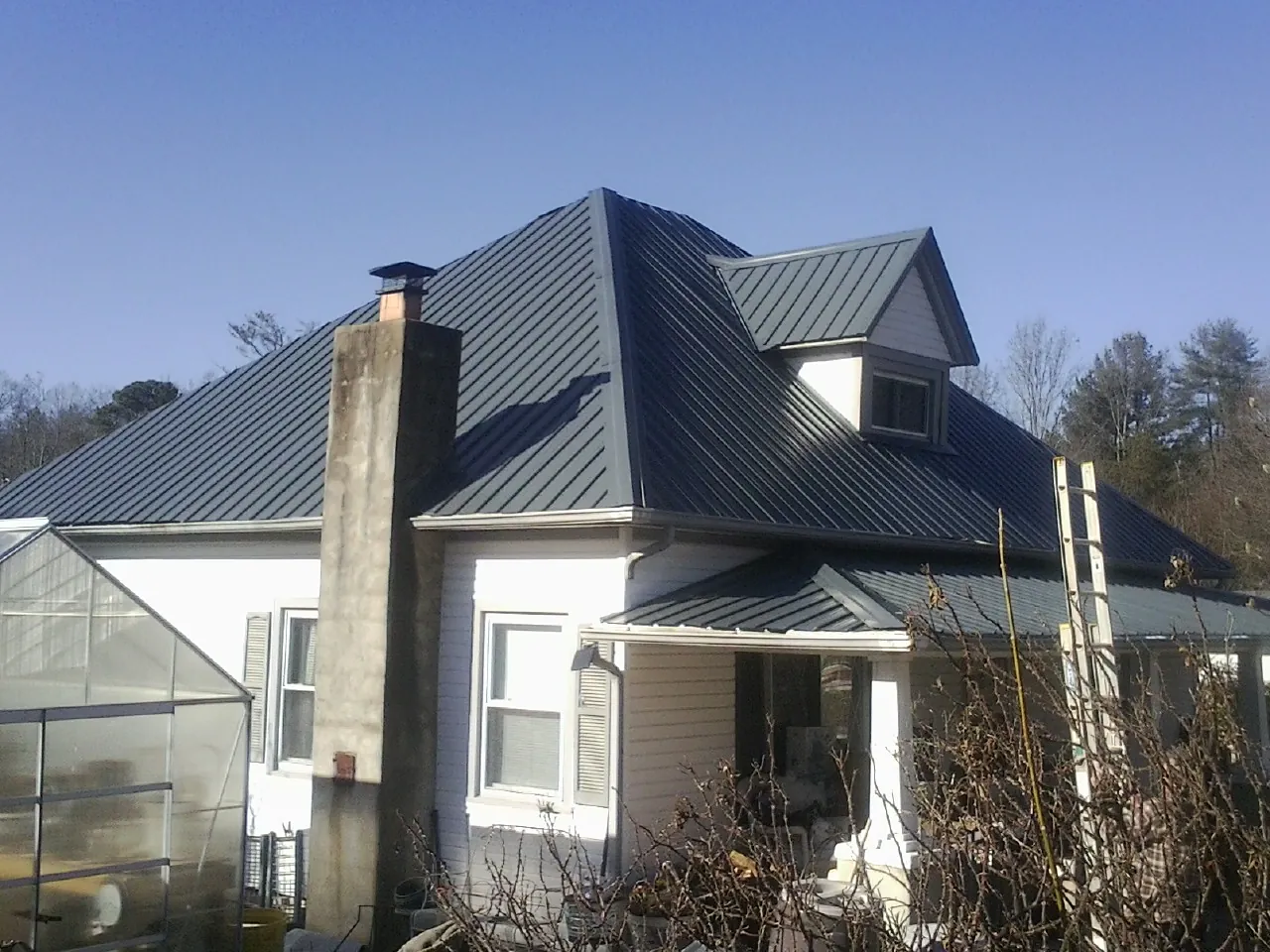 Dark blue standing seam metal roof on a white farmhouse with dormer — Slate & Tile Roof Repair by Roofing Brothers in Ballston Spa