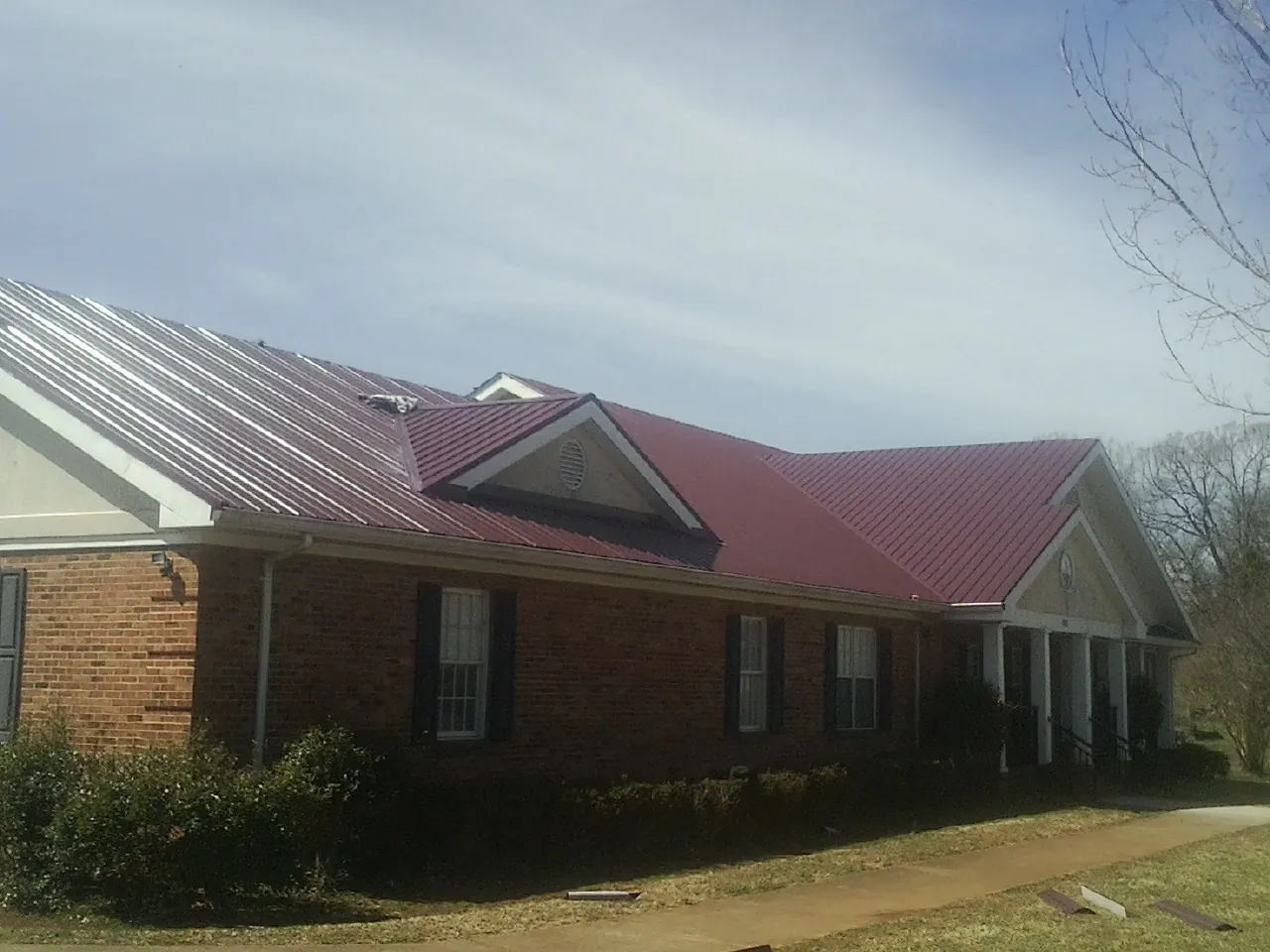 Red metal roof with gabled entries on a long brick building, from a Hail Damage Roof Repair job in Ballston Spa