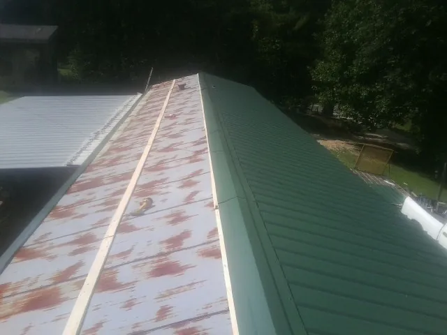 Old rusted panels beside newly installed green metal roofing — Wind Damage Roof Repair by Roofing Brothers in Ballston Spa