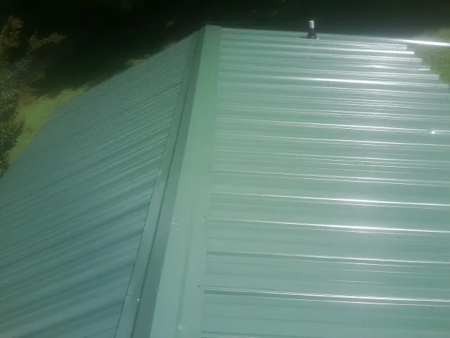 New green metal panels meeting at the ridge of a roof — Flat Roof Repair work by our crew in Ballston Spa