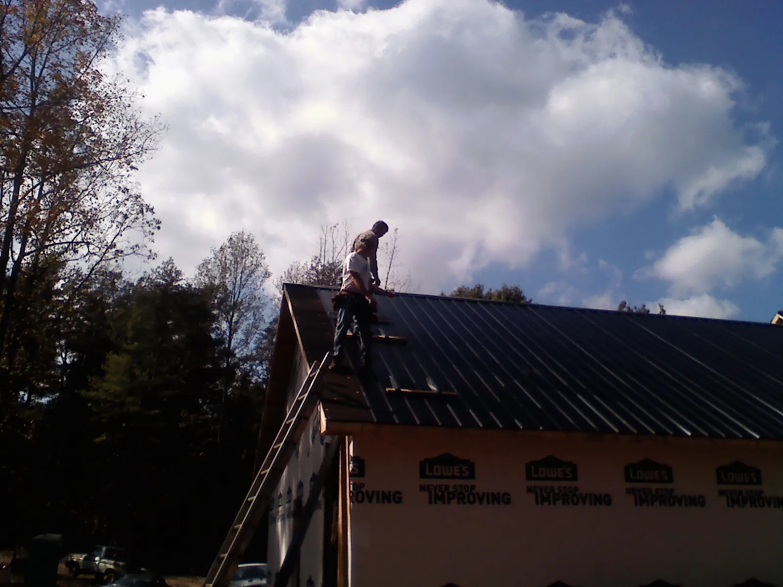 Roofer fastening dark metal panels high against a cloudy sky, from a Roof Inspection job in Ballston Spa