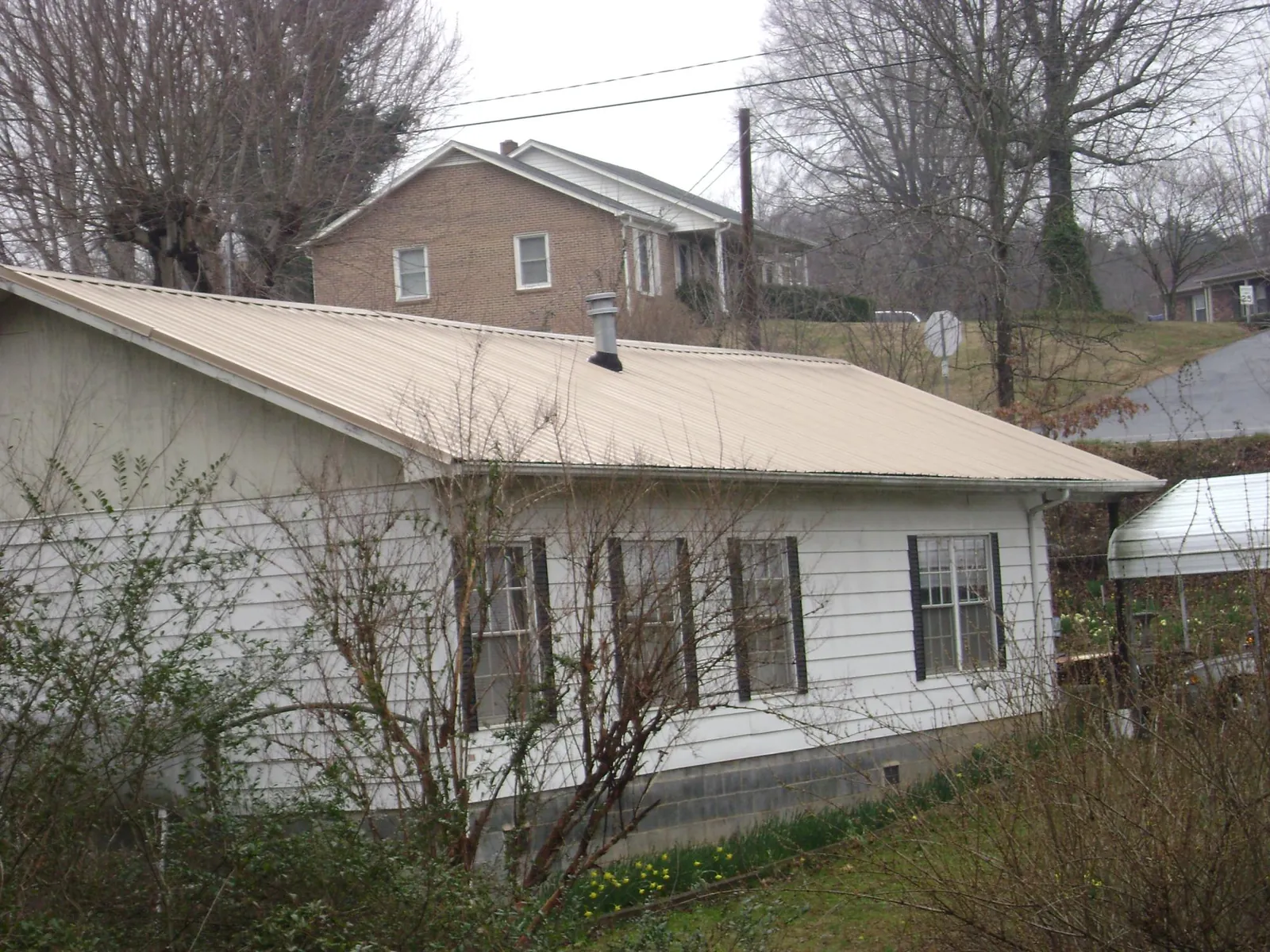 Tan metal roof on a white sided house set into a hillside — Commercial Roofing by Roofing Brothers in Ballston Spa